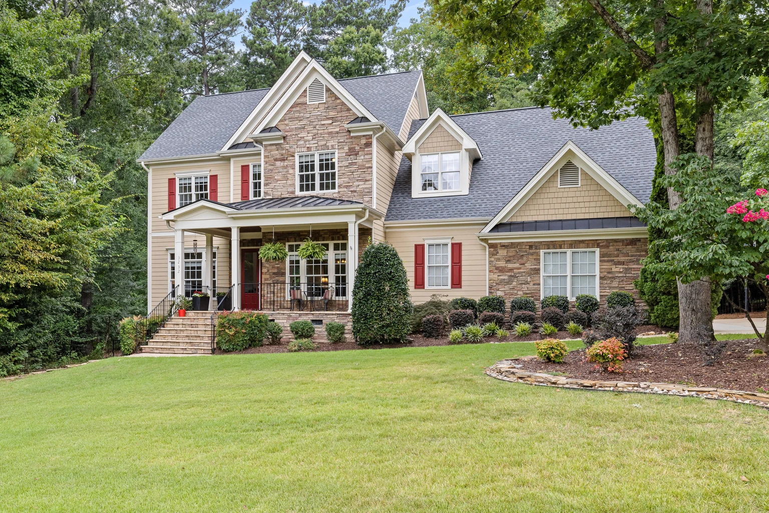 Two-story home framed by a green lawn, mature trees, and landscaped garden beds