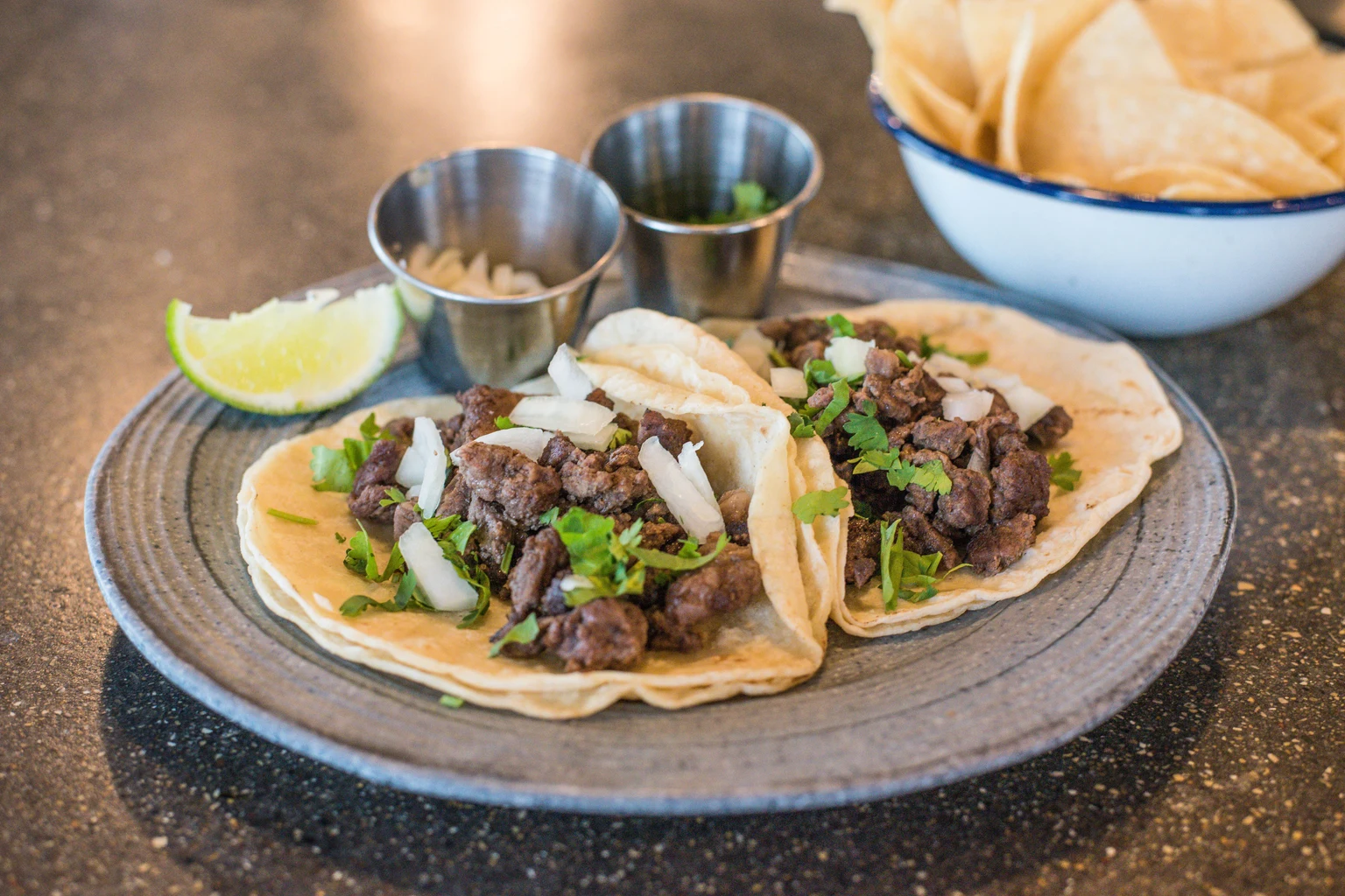 Beef tacos with onion, cilantro, lime, and tortilla chips on a restaurant table
