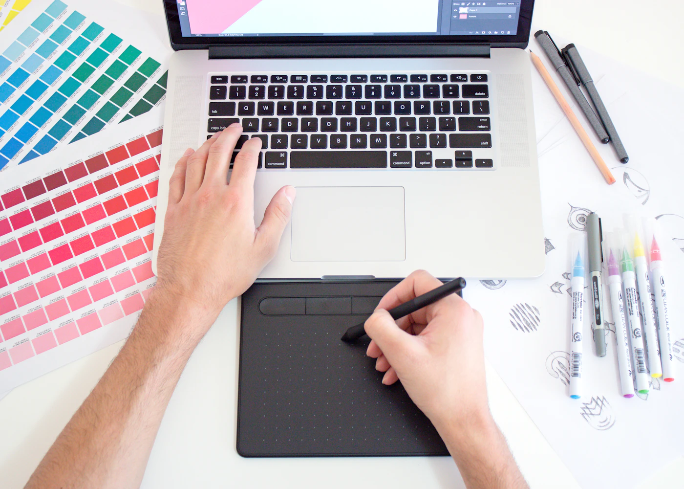 Designer using a drawing tablet beside a laptop and color swatches
